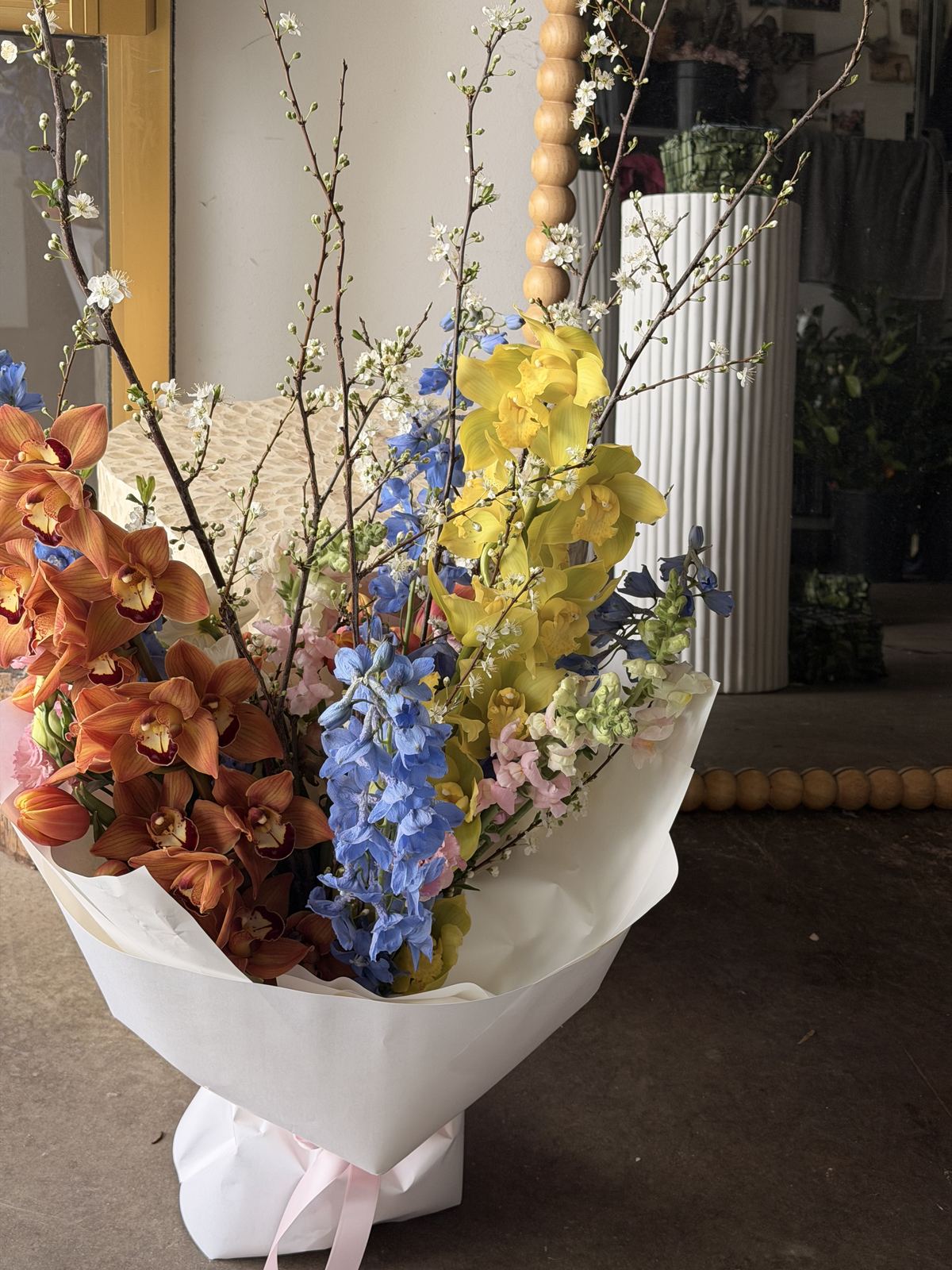Extra-large anniversary bouquet of orange and yellow cymbidium orchids, blue delphinium and blossom branches by Sugar Bee Flowers