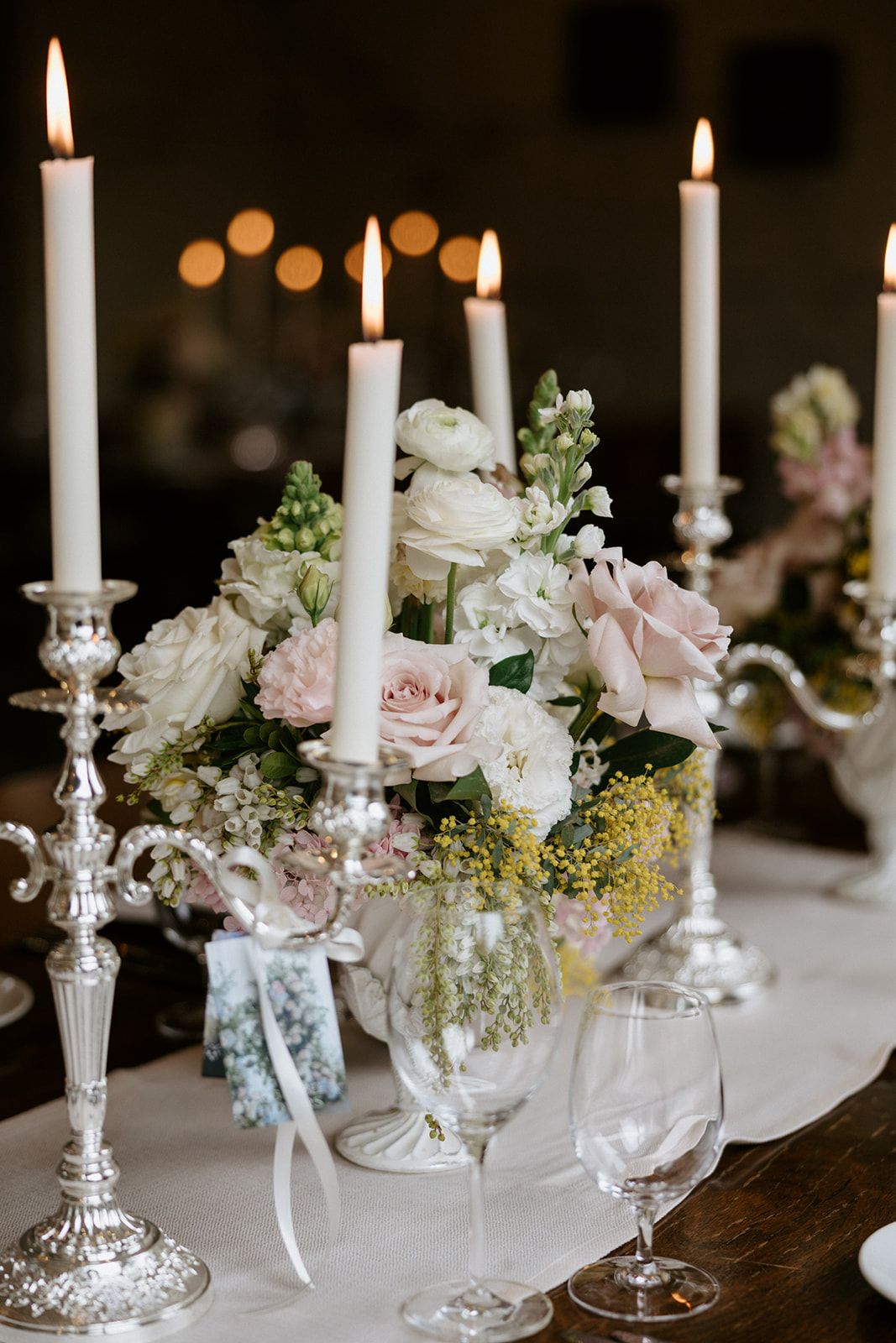 Candlelit centrepiece of white ranunculus, blush roses and mimosa at the Stones Unveiling