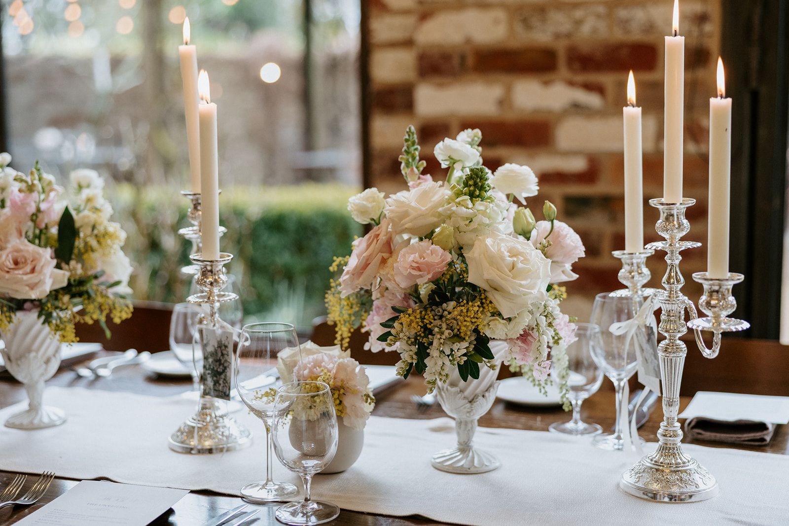 Table setting with silver candelabras and blush and white floral urns at The Stables Restaurant